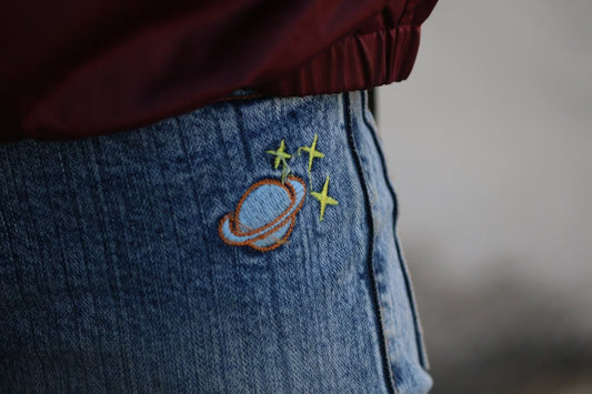 Blue jeans with an embroidered planet and stars.