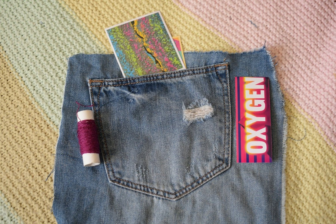 A denim pocket containing a colorful card, beside purple thread and an Oxygen sign