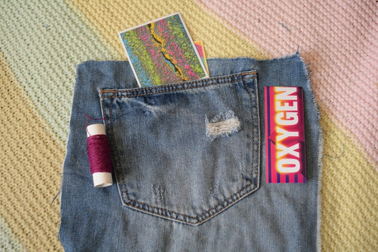 A denim pocket containing a colorful card, beside purple thread and an Oxygen sign