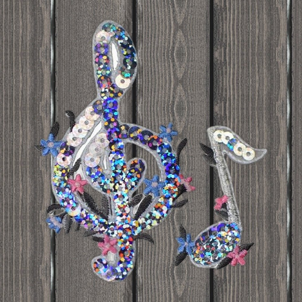Two sequin music patches: a G clef and a single musical note, on a wood background