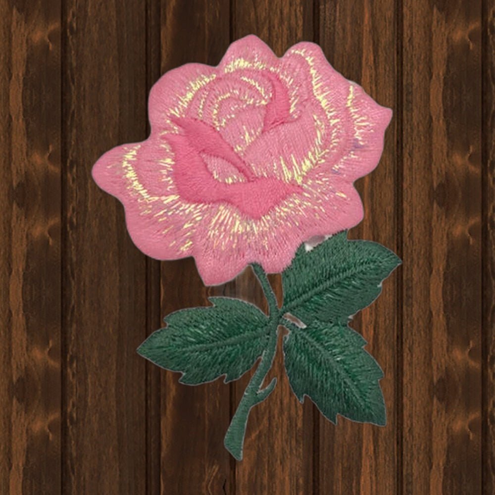 Pink shimmery rose embroidered patch, 3-1/8 inches, on a wood background
