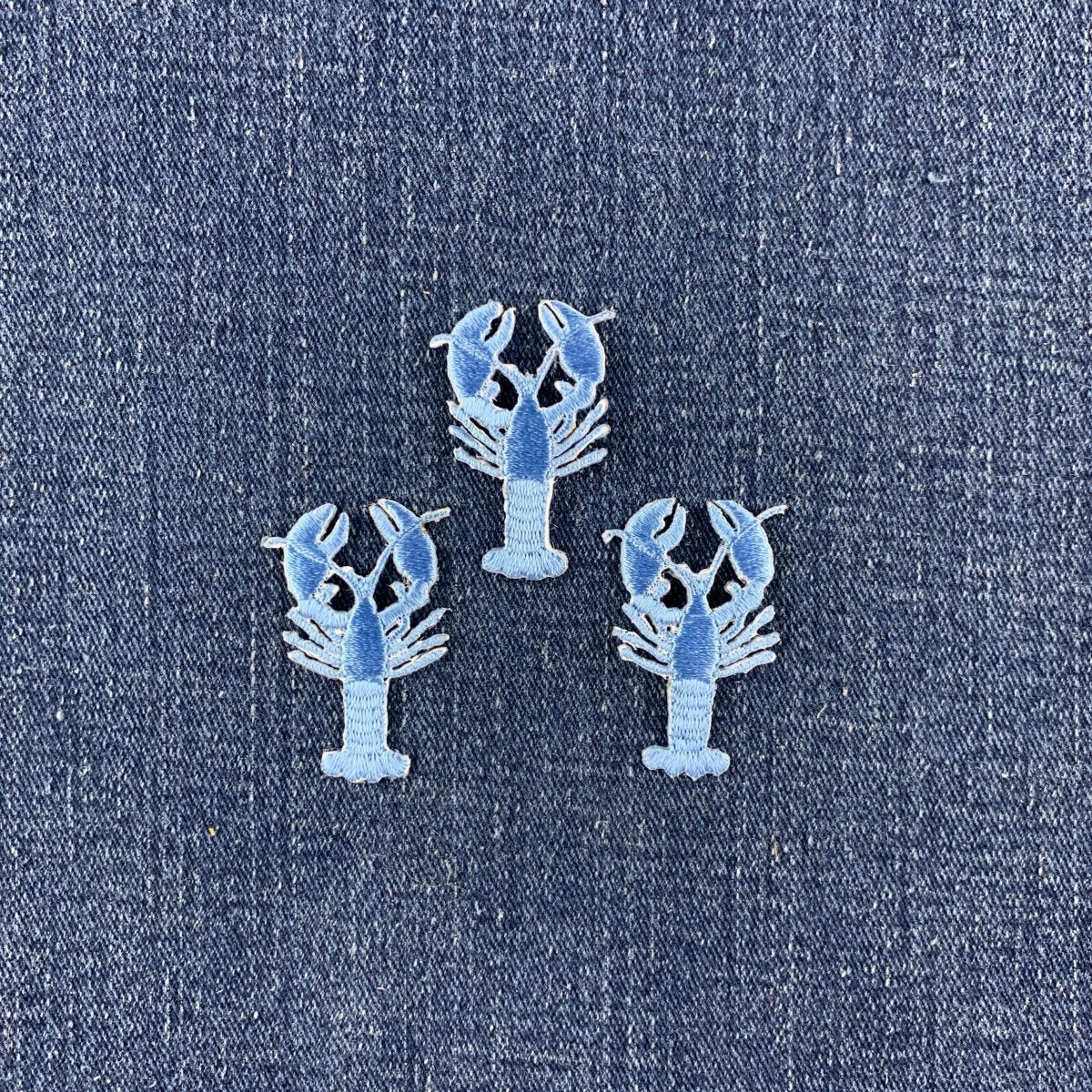 Three lobster-shaped patches in light blue, arranged on a textured blue denim fabric background.