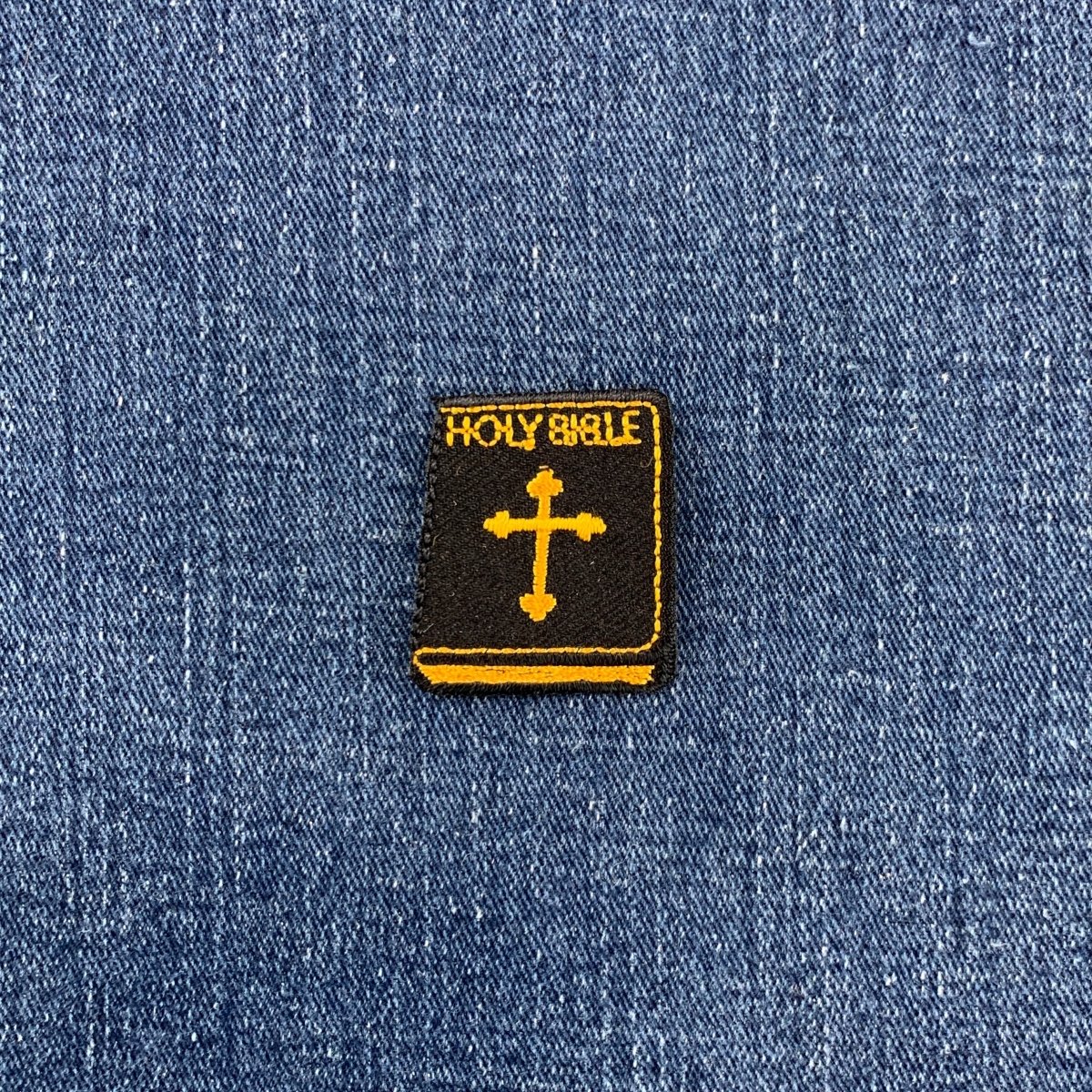 Embroidered patch of a 'Holy Bible' with a cross on blue denim fabric.