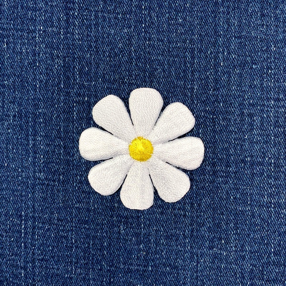 White embroidered daisy flower patch on blue denim fabric