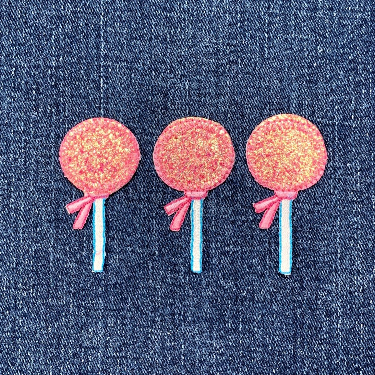 Three pink lollipop-shaped patches against a denim background
