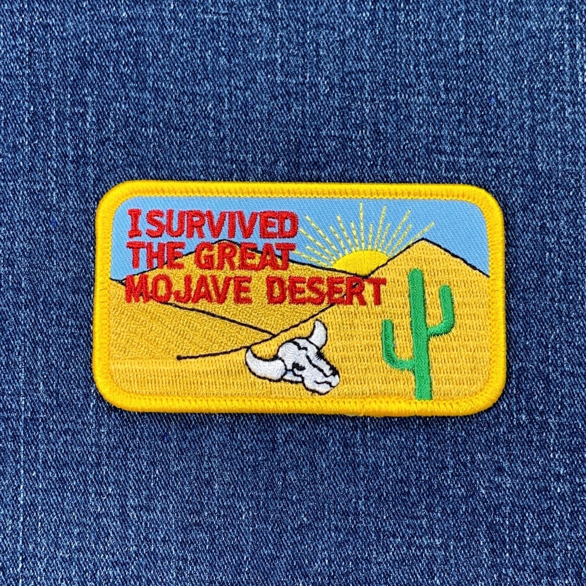 Embroidered patch with desert scene and text 'I Survived the Great Mojave Desert' on a blue denim background.