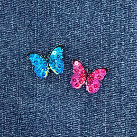 Two butterfly-shaped sequin patches, one blue and one pink, on a denim background.