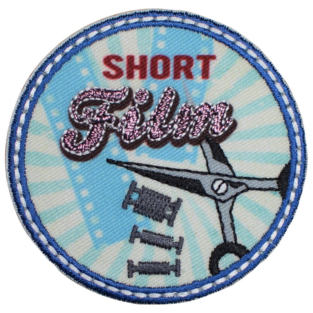 A circular applique patch with the words 'SHORT FILM' written in the center, accompanied by images of film reels and scissors. The patch is designed for iron on application.